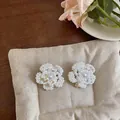 Vista macro detallada de elegantes pendientes de flores de perlas en un suave cojín de color crema - Blanco