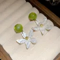 Detail view of elegant white resin flower earrings with green beads in velvet box - White-Green