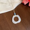 Primo piano di un ciondolo ad anello in acrilico marmorizzato bianco su cordino crema. - Pendaglio Quadrato / Bianco