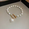 Détail d'un bracelet en perles élégant avec pendentif coeur en zircon et fermoir OT doré. - Style Perle avec Boucle OT et Coeur en Strass