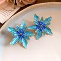 Detailed macro shot of blue enamel flower earrings with gold trim on a ceramic plate - Blue