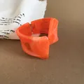 Primer plano de un brazalete de resina veteada naranja con diseño geométrico retorcido - Naranja