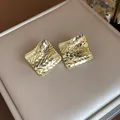 Close-up detail of golden rhombus stud earrings featuring a textured diamond-cut surface design - Gold