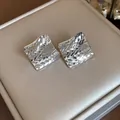 Close-up of silver rhombus stud earrings with elegant geometric diamond-cut pattern texture. - Silver