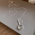 Detailed view of a vintage silver necklace featuring a unique magnifying glass and key pendant. - Silver