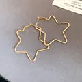 Detailed view of oversized 18k gold plated star hoop earrings on a grey background. - Gold