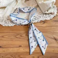 Detailed close-up of a resort style floral fabric scarf necklace with a golden ring - Gold Ring Buckle / Blue White Print