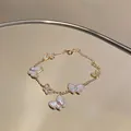 Detailansicht eines goldfarbenen Armbands mit funkelnden Zirkon- und Muschel-Schmetterlingen. - Gold-Weiß