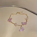 Detail eines rosa Schmetterlingsarmbands mit funkelnden Zirkonia auf einer goldfarbenen Kette. - Gold-Lila