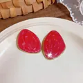 Primo piano di orecchini a lobo geometrici irregolari in smalto rosso con bordi dorati. - Rosa Rosso