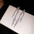 Close-up of sparkling zircon tassel earrings on a textured jewelry box - Square Tassel / Silver