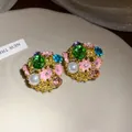 Close-up view of vintage floral stud earrings featuring vibrant crystals and pearls - Gold / Pink