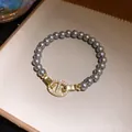 Detailansicht eines eleganten grauen Perlenarmbands mit einem goldglänzenden Schmuckelement - Strass-besetzter Ankerketten-Stil / Gold with Gray Pearl