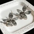 Primo piano di orecchini a fiore in metallo con petali testurizzati su un vassoio bianco. - Tops / Argento