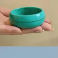 Primer plano de un brazalete redondo ancho de acrílico jaspeado verde azulado en la mano - Tinte Cian