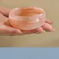 Detalle de un brazalete ancho de acrílico con patrón jaspeado melocotón sostenido en mano. - Rosa Jaspeado