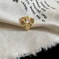 Macro view of a textured gold heart-shaped ring on a rustic beige fabric background. - Open Ring / Gold