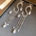 Macro vista di orecchini metallici a forma di S con eleganti nappe di perle bianche. - Argento
