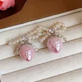 Close-up detail of sweet pearl bow earrings featuring dangling pink strawberry charms - Silver Post Stud (57)