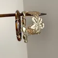 Detailed view of three vintage-style flower and resin bracelets hanging on a wooden stick - Tortoiseshell Resin Bangle Set / Gold Brown
