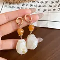 Close-up of marbled resin irregular geometric earrings with golden hoops and amber beads - Beige
