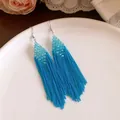 Gros plan sur des boucles d'oreilles bohèmes à perles bleues et longues franges. - Style de Pompon Bohème / Bleu
