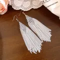 Détail rapproché de boucles d'oreilles bohèmes à pampilles et perles sur fond de bois - Style de Pompon Bohème / Blanc