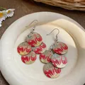 Dettaglio di orecchini tondi in smalto con stampe floreali rosse e farfalle blu vivaci - Rosso