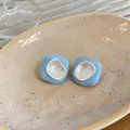 Gros plan de boucles d'oreilles géométriques en émail bleu ciel sur plateau en céramique - Bleu