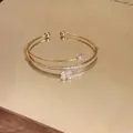 Dettaglio di bracciale rigido dorato a doppio strato con zirconi e quadrifoglio - Stile Quadrifoglio a Quattro Foglie / Oro