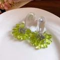 Close-up of green resin teardrop tassel earrings with silver needles on a white plate. - Green
