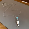 Detailed macro view of matte silver fish pendant necklace featuring a turquoise bead - Silver