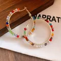 Close-up of gold hoop earrings with vibrant colorful glass beads on a fabric background - Round / Silver Needle / Colorful