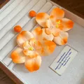 Detailed view of orange raffia fabric flower earrings inside a cream jewelry tray. - Orange
