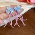 Primo piano di orecchini a lobo con fiori blu e lunghe nappe di graziose perline rosa - Blu-Rosa