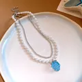 Detailed view of a layered necklace with white pearls and a blue resin grape pendant. - White And Blue Necklace