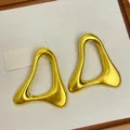 Gros plan de boucles d'oreilles géométriques irrégulières en métal doré sur fond de toile - Clous Géométriques Creux Irréguliers / Or
