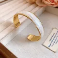Detailed view of an 18K gold-plated open bangle featuring an elegant white wave enamel finish - 18K Gold Plated / Brown