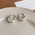Detail view of U-shaped silver hoop earrings with quilted texture on a beige plate. - Ear Buckle / Silver
