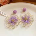 Macro view of purple raffia flower earrings with intricate gold wireframe detailing. - Purple