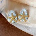 Detail-Makroansicht von goldenen Seestern- und blauen Muschelohrringen auf Seide - Silber-Ohrstecker-Stil / Gold-Blau