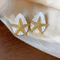 Makro-Detail von goldenen Seestern- und weißen Muschelohrringen auf Seidenstoff - Silber-Ohrstecker-Stil / Gold-Weiß
