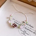 Détail d'un bracelet tissé avec cristal, fleurs en résine et petits grelots décoratifs. - Blanc-Rose-Vert