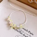 Détail macro d'un bracelet à fleurs en résine et cloches sur cordon blanc tressé - Blanc-Vert