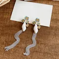 Detail view of long silver tassel earrings featuring blue and gold enamel flowers. - Blue-White