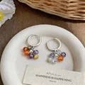 Detailed macro view of colorful faceted zircon bead hoop earrings on a textured plate. - Hoop Buckle Style / Colorful