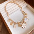 Gros plan d'un collier doré avec breloques coquillages, fleurs et animaux marins - Or-Blanc