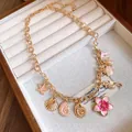 Gros plan détaillé d'un collier vintage émaillé avec des pendentifs coquillages et fleurs - Or-Rose