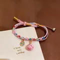 Close-up of hand-woven colorful rope bracelet with beads and pink charm on white card - Pink Blue Prosperity Tag Style