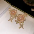 Detailed view of gold-plated flower stud earrings with pink stones and pearls in a box. - Gold